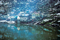Reflection of snowy houses on rocky hill in lake