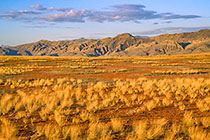 dry grass sandy valley + mts at sunset