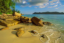 rocks on beach with wave effect + sea + Curieuse island after sunrise