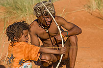 bushman teaching boy bow & arows on red sand dunes