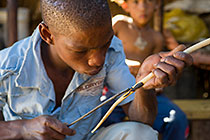 bushman boy burning drawing on bow near fire