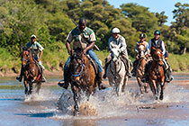 people on horses cantering in river