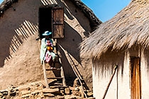 woman with baby sitting on ladder in front of village house