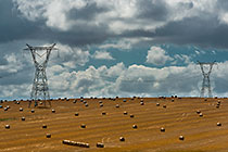 clouds & electrical pilones over wheat field with hay rolls
