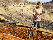Paul watering Hugel garden boxes filled with wooden branches & chips