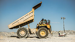 worker near lighting trailer & 90 T truck offloading waste rocks