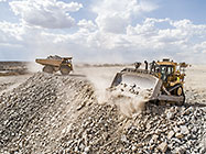 bulldozer & 90 T trucks offloading rocks on top of waste pile