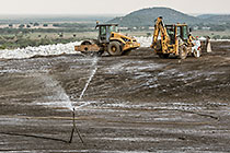 arsenic waste site | water sprayers | workers near digger loader & roller compactor