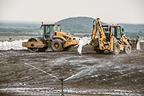 arsenic waste site | water sprayers | workers near digger loader & roller compactor