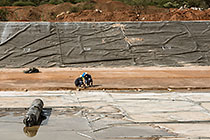 workers laying concrete on top of thick plastic lining in new water bassin