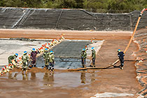 workers laying concrete on top of thick plastic lining in new water bassin