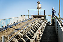 worker at the end of conveyor belt on top of tailings