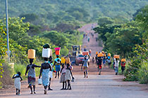 people carrying water on head walkking on road