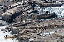 boat & man sitting near waterfall between rocks at sunrise