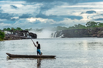 fisherman on boat on river in front of waterfall